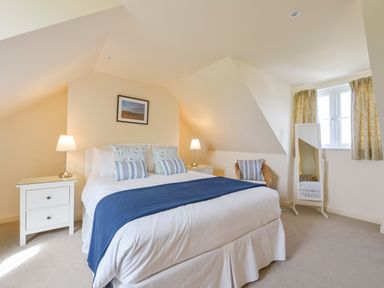 A bedroom with a bed with blue and white bedding two bedside tables with lamps a chair a full length mirror and a window with curtains at Duffield in St Anns Chapel