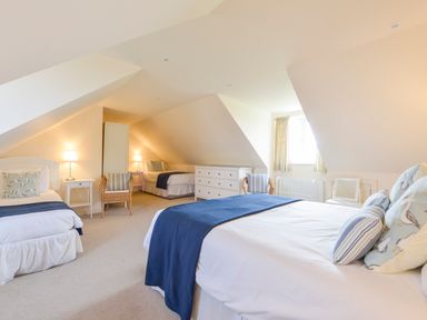 A bedroom with three beds two wicker chairs a white dresser and a window with curtains at Duffield in St Ann's Chapel