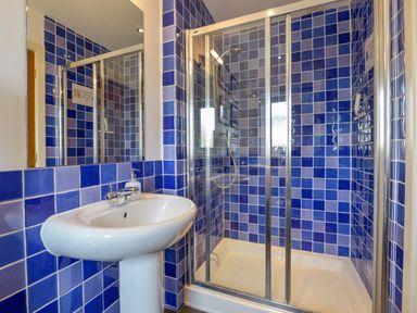 A bathroom with a white pedestal sink and a shower with blue tiled walls and glass doors at Duffield in St Ann's Chapel