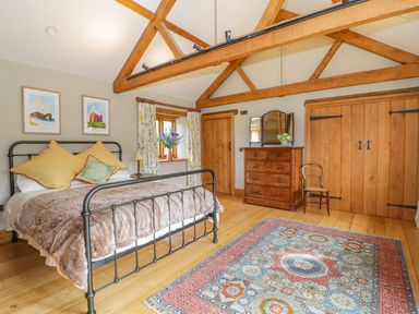 A bedroom with a metal bed frame wooden dresser mirror wooden doors and a colorful rug at Middle Farm Annex in Long Bredy