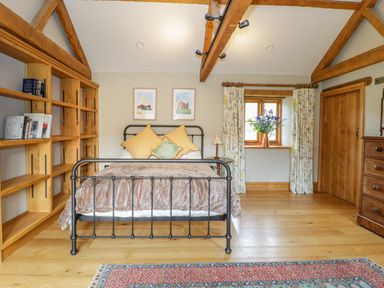 A bedroom with a metal bed frame, wooden shelves, a floral curtain, a wooden dresser, and exposed ceiling beams at Middle Farm Annex in Long Bredy