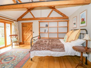 A bedroom with a metal bed frame wooden shelves a wooden door a chair next to glass doors and a patterned rug at Middle Farm Annex in Long Bredy