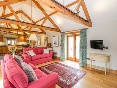 A living room with red sofas wooden beams a patterned rug and a small wall-mounted television at Middle Farm Annex in Long Bredy