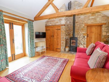 A living room with red sofa and striped cushions a fireplace a patterned rug doors with wooden beams and floral curtains at Middle Farm Annex in Long Bredy