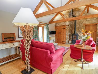 A living room with wooden beams red sofas a floor lamp wooden table and a stone fireplace at Middle Farm Annex in Long Bredy