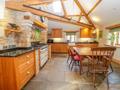 A kitchen with wooden cabinets and chairs a dining table a stove and stone walls at Middle Farm Annex in Long Bredy