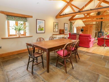 A dining area with wooden table and chairs next to a living room with red sofas and wooden beams at Middle Farm Annex in Long Bredy