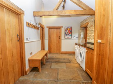 A utility room with wooden doors a bench coat hooks a washing machine and a dryer at Middle Farm Annex in Long Bredy