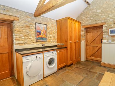 A laundry room with stone walls wooden cabinets a washing machine a dryer and a wooden door at Middle Farm Annex in Long Bredy