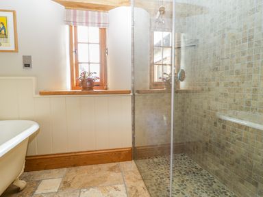 A bathroom with a bathtub on the left a window with a potted plant in the middle and a glass-enclosed shower with pebble floor tiles on the right at Middle Farm Annex in Long Bredy