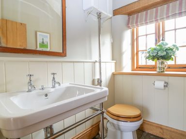 A bathroom with a white sink a toilet with a wooden seat a window with flowers on the sill and a mirror at Middle Farm Annex in Long Bredy