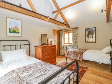 A bedroom with two single beds a wooden dresser with a mirror and flowers a window with curtains and exposed wooden beams at Middle Farm Annex in Long Bredy