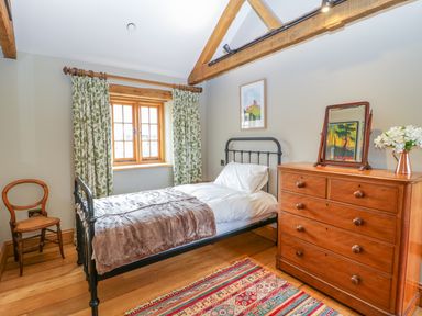 A bedroom with a single bed a wooden chair a wooden dresser with a mirror curtains on a window and a colorful rug at Middle Farm Annex in Long Bredy