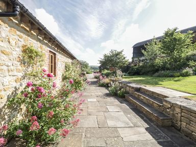 A stone building with windows and flowers along a paved pathway next to stone steps and greenery at Middle Farm Annex in Long Bredy