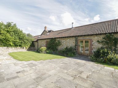 An exterior view of a stone building with a tiled roof a grass lawn and paved patio with shrubs and plants at Middle Farm Annex in Long Bredy