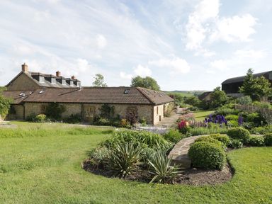A garden with shrubs and flowers in front of stone buildings with tiled roofs at Middle Farm Annex in Long Bredy
