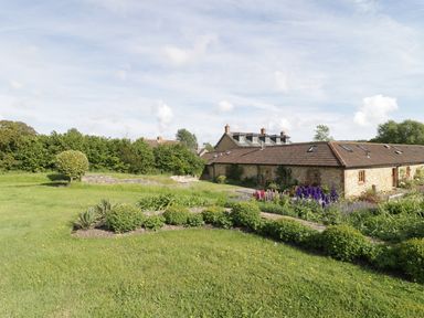 A garden with bushes flowers and grass outside a stone house with a tiled roof at Middle Farm Annex in Long Bredy