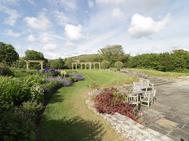 A garden with a stone patio with wooden benches and chairs at Middle Farm Annex in Long Bredy