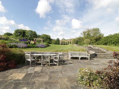 An outdoor patio with wooden table and chairs stone steps and garden with flowers and trees at Middle Farm Annex in Long Bredy