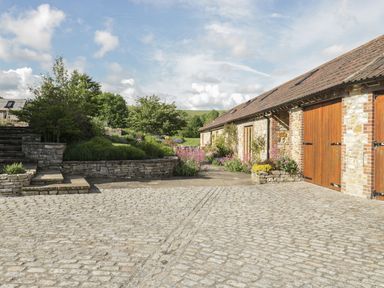 A stone-paved courtyard with stone steps and a garden next to a building with wooden doors at Middle Farm Annex in Long Bredy