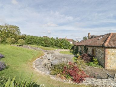 A garden with stone patio area wooden table and chairs and a stone building at Middle Farm Annex in Long Bredy