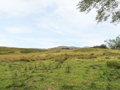 A grassy landscape with hills and sparse vegetation under a partly cloudy sky at New Peny in Llandrindod Wells
