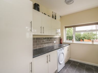 A utility room with white cabinets a black countertop a washing machine and a window at New Peny in Llandrindod Wells