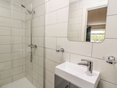 A bathroom with a shower area a sink a faucet a mirror and a window visible in the reflection at New Peny in Llandrindod Wells
