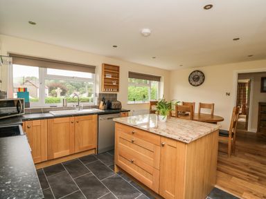 A kitchen with a wooden island, dining table with chairs, and windows overlooking greenery at New Peny in Llandrindod Wells