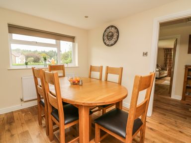 A dining room with a wooden table and six chairs near a window showing a view outside at New Peny in Llandrindod Wells
