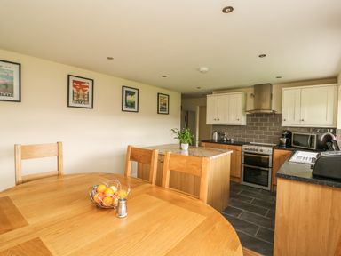 A kitchen with a wooden dining table fruit bowl and salt shaker an island with a plant and kitchen appliances at New Peny in Llandrindod Wells