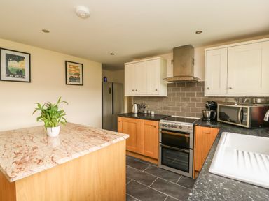 A kitchen with a marble island, wooden cabinets, stainless steel appliances, and framed pictures on the wall at New Peny in Llandrindod Wells