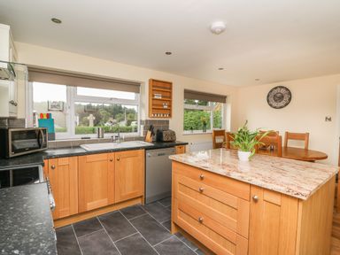 A kitchen with wooden cabinets island with a plant dining table and chairs at New Peny in Llandrindod Wells