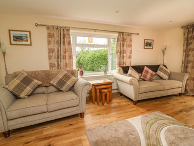 A living room with two beige sofas each with cushions and a set of nesting wooden tables by a window at New Peny in Llandrindod Wells