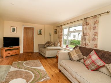 A living room with two sofas a television on a wooden stand a wooden door a patterned rug and large window at New Peny in Llandrindod Wells