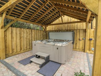 A covered hot tub with steps on a paved floor surrounded by wooden fencing at New Peny in Llandrindod Wells