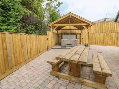 A paved outdoor area with a wooden picnic table and a covered hot tub at New Peny in Llandrindod Wells