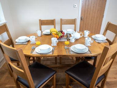 A wooden dining table set with white dishes cups glasses of orange juice and a fruit basket at New Peny in Llandrindod Wells
