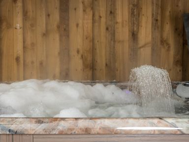 A bubbling hot tub with water flowing from a spout against a wooden wall at New Peny in Llandrindod Wells