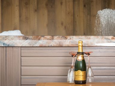 A bottle of Taittinger champagne with two upside down glasses tied to it in front of a hot tub with water splashing and foam at New Peny in Llandrindod Wells