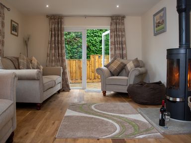 A living room with two armchairs a wood stove a rug and an open door to a garden at New Peny in Llandrindod Wells