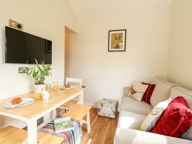 A small dining area with a wooden table set with plates and orange juice beside a beige sofa in a living room at Bramble in Banham