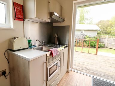 A compact kitchen with a sink, toaster, stove, microwave, and knife set next to a sliding door leading to a garden at Bramble in Banham