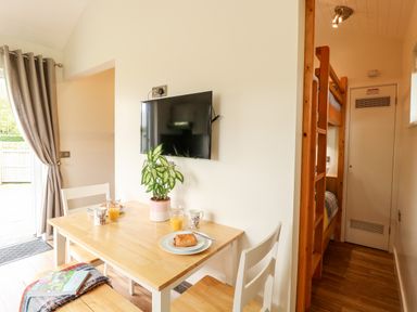 A dining area with a wooden table and chairs a mounted TV and bunk beds in a small room at Bramble in Banham