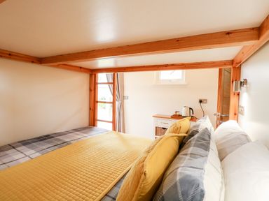A bedroom with a bed with yellow and plaid bedding a wooden frame window with curtains and a small cabinet with a kettle at Bramble in Banham