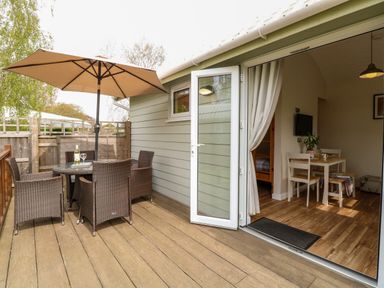 An outdoor patio with a table and four chairs under an umbrella next to an open door leading to a dining area at Bramble in Banham