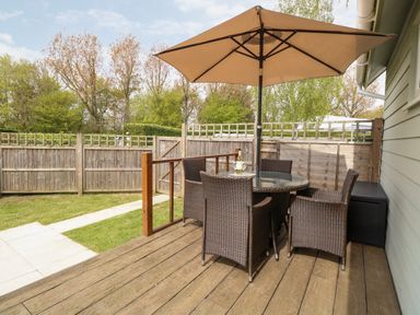 An outdoor patio with a round table under an umbrella and four wicker chairs at Bramble in Banham