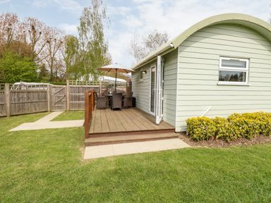 A garden patio with a table umbrella chairs and wooden decking outside a light green cabin at Bramble in Banham