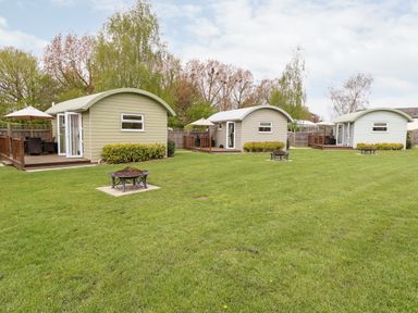 Three small cabins with curved roofs on a grassy area with fire pits and wooden decks at Bramble in Banham