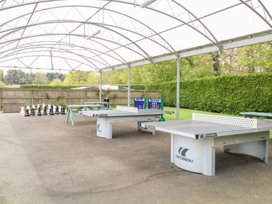 An outdoor covered area with two ping pong tables giant chess set picnic benches and connect four game at Bramble in Banham